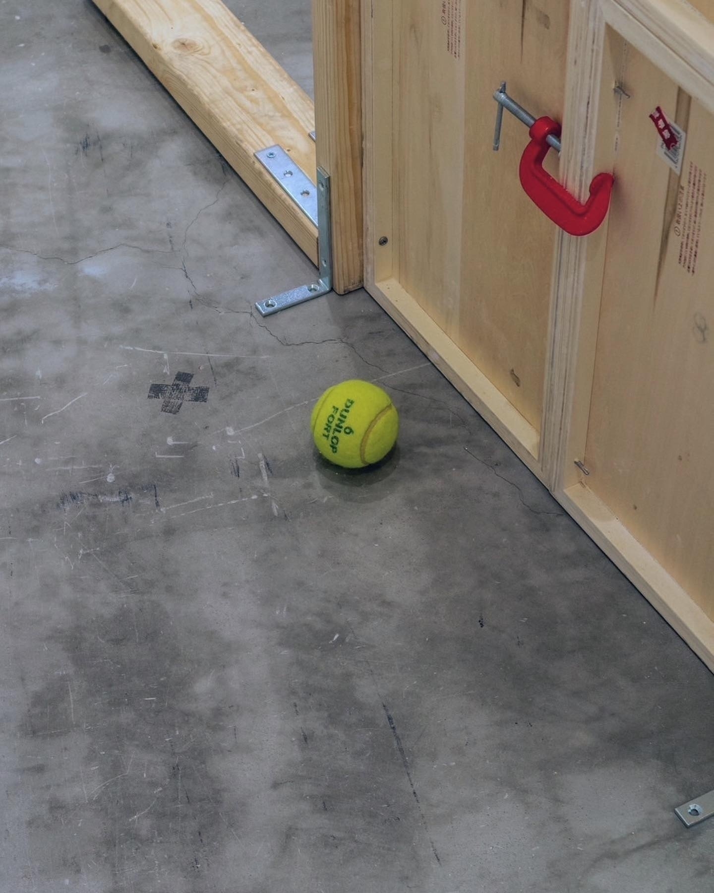 A tennis ball is on a concrete floor near a wooden structure.